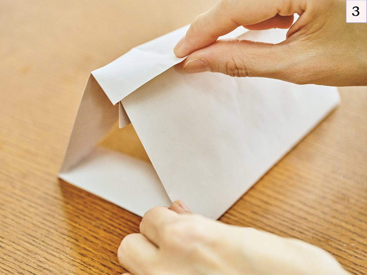 3等分の折り目に合わせて三角形に形を整え、上部にできた袋 状の部 分に、手前の2cm部分を差し込みます。【かわいいおうちボックスの作り方】