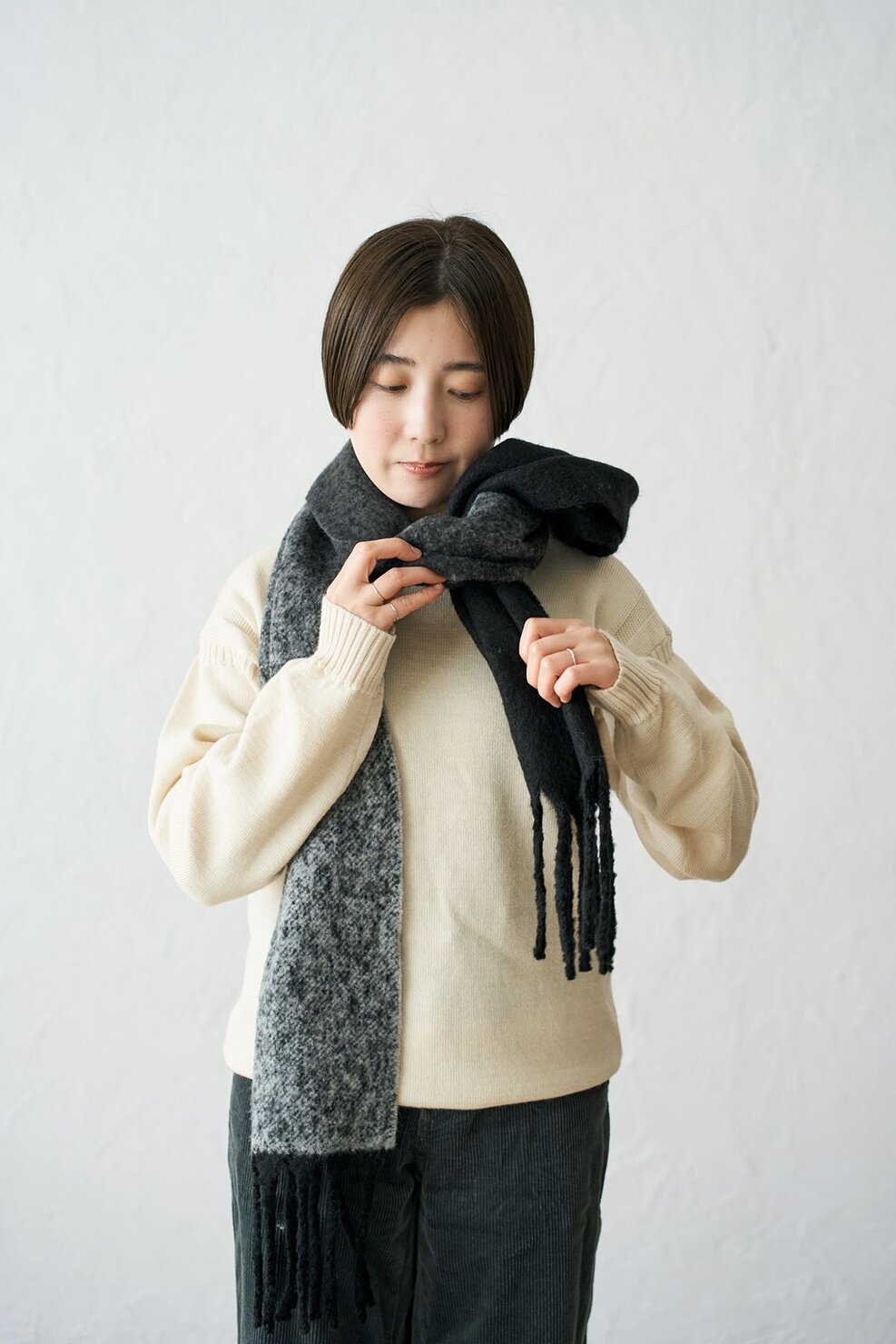 マフラーを首の前からかけて後ろでクロスし、両端を前に垂らして、片方のマフラーを輪っかの内側に通す