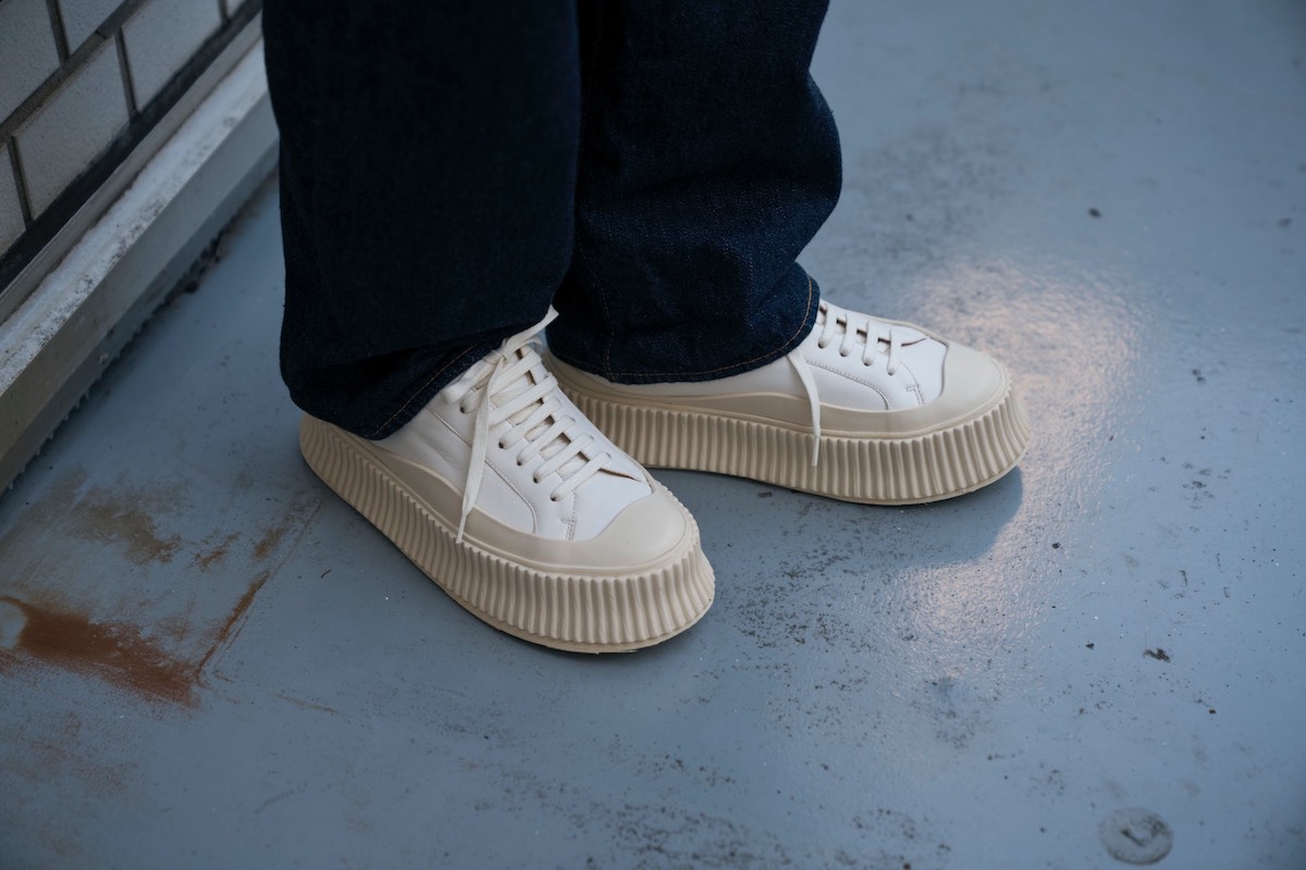 濃紺のデニムパンツに白のレザースニーカーを合わせた足もとのコーディネート