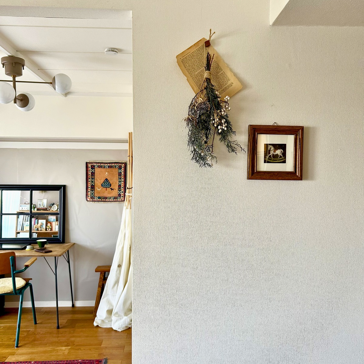 手前:小さな絵とドライフラワー、後ろの部屋:小さなラグを壁掛けにした写真