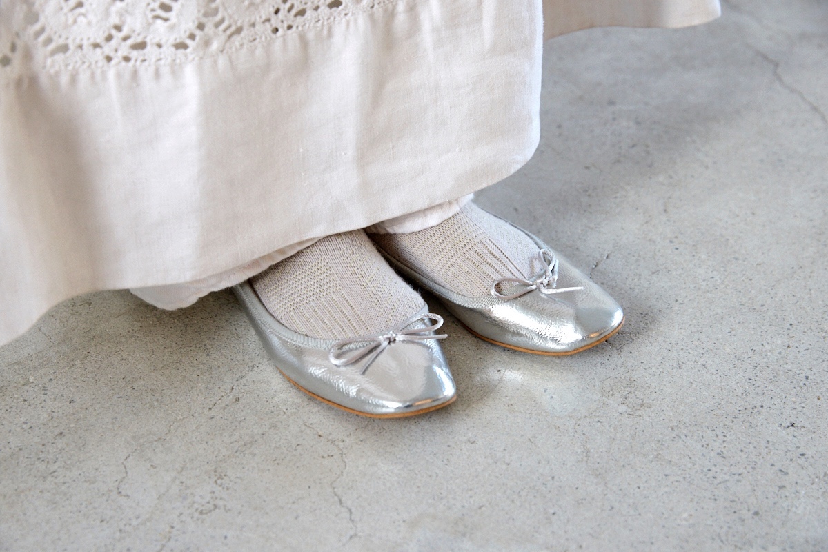 白の装いに映えるシルバーのバレエシューズとソックスを合わせた軽やかな足もと