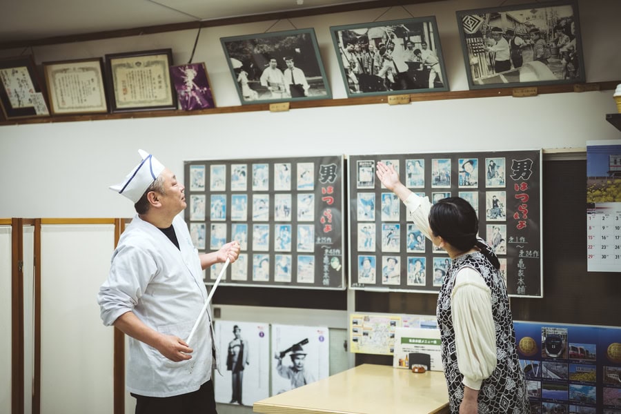 亀家本舗の店内で昔の写真を見る甲斐さん