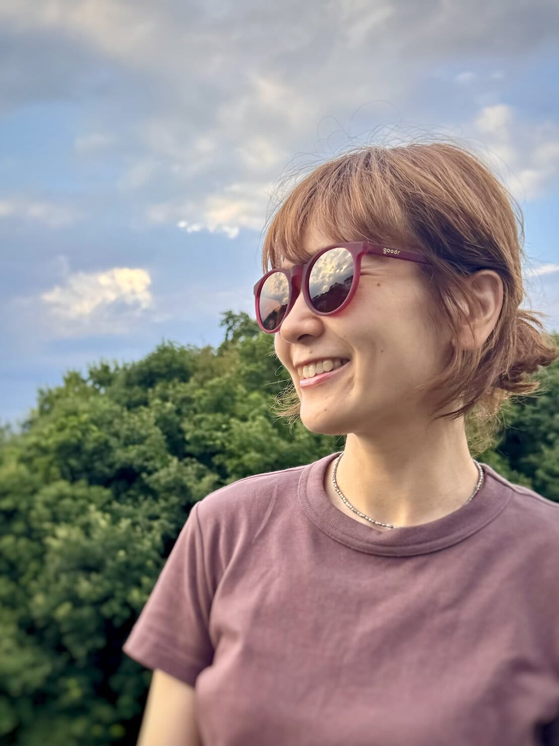 goodrのサングラスを掛けて横向きで森の前に立っている