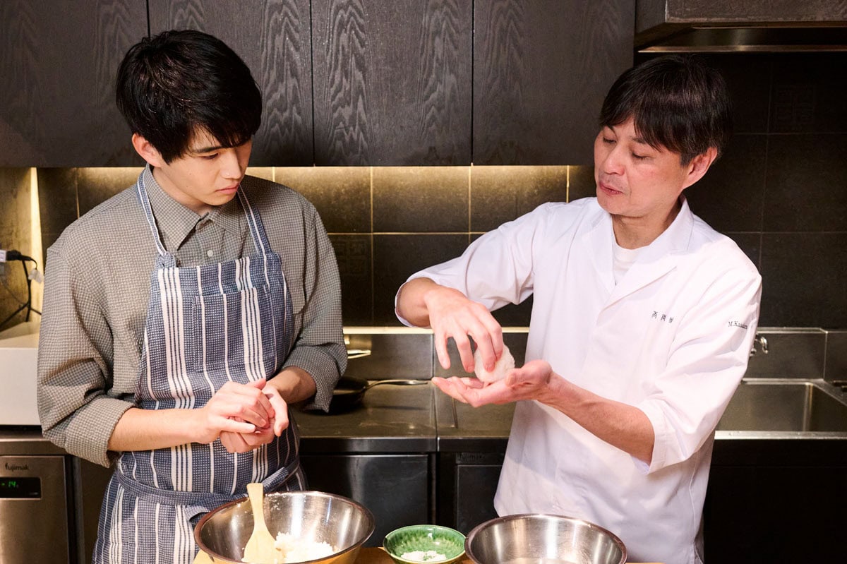 俳優・中沢元紀さんが、日本料理店「賛否両論」を営む料理人・笠原将弘さんから塩むすびのむすび方について学んでいる様子